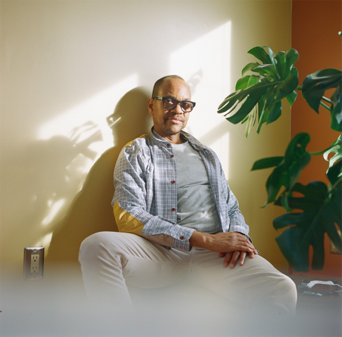 Lyle Ashton Harris sitting against a wall next to a plant